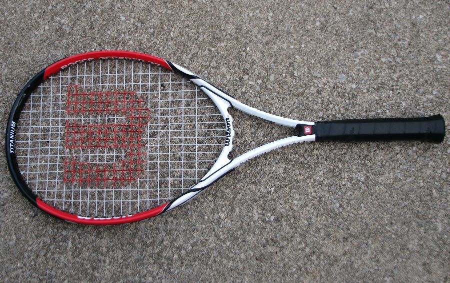 A Wilson tennis racket with black handle and red head.
