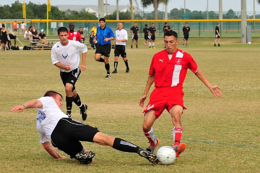 An US soccer player in white jersey tackling his opponent in red jersey.