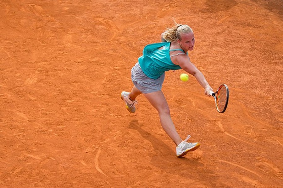 A female tennis player in blue jersey playing on clay court.