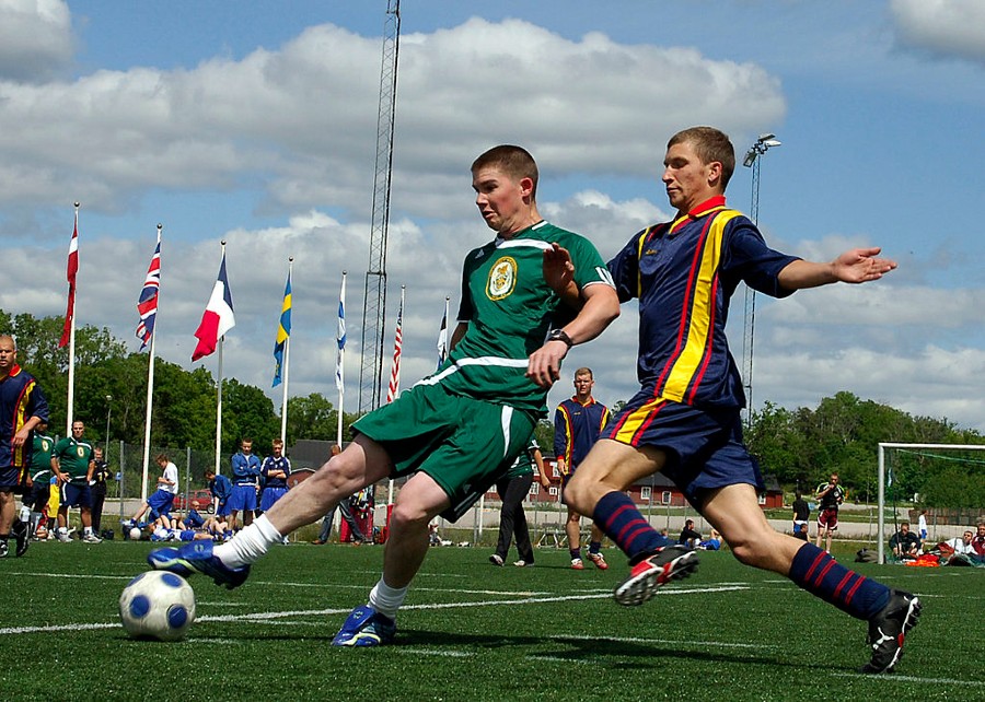Two soccer players running for a ball in a green stadium.